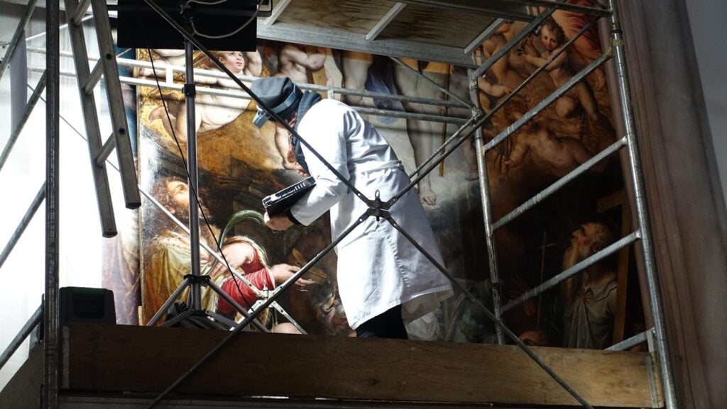 Man in white long sleeve shirt holding black and white corded power tool in a commercial attic work to find hidden mold.